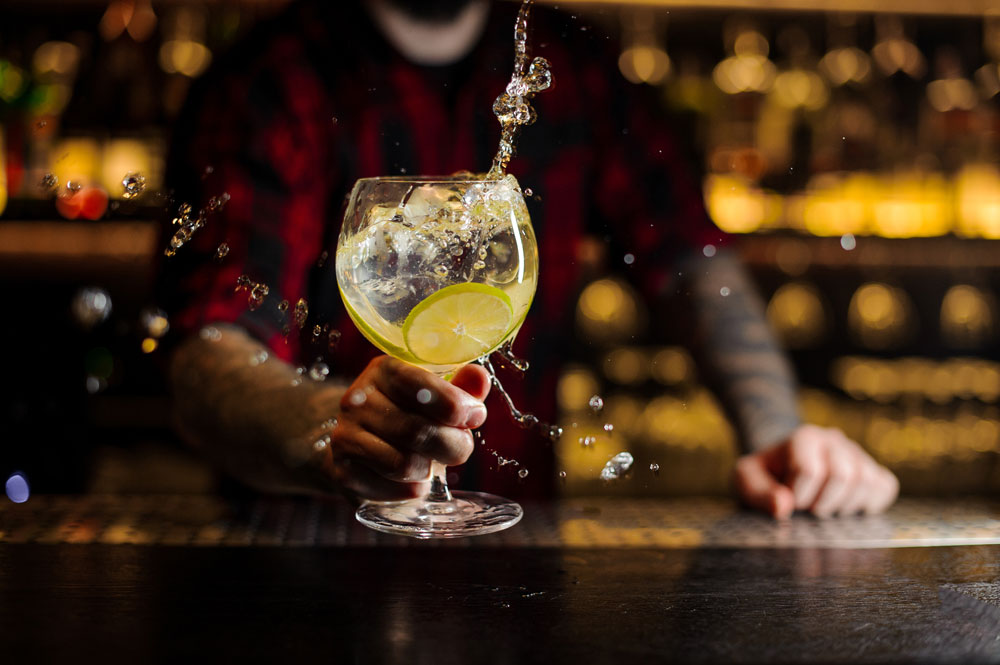 Gin Distillery selling Gin and Merchandise Gin cocktail being swirled on bar by bartender in checked shirt with tattoos